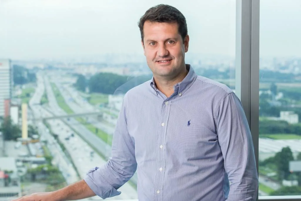 Marcelo França, de terno azul e braços cruzados, com o logo da Celcoin no canto.